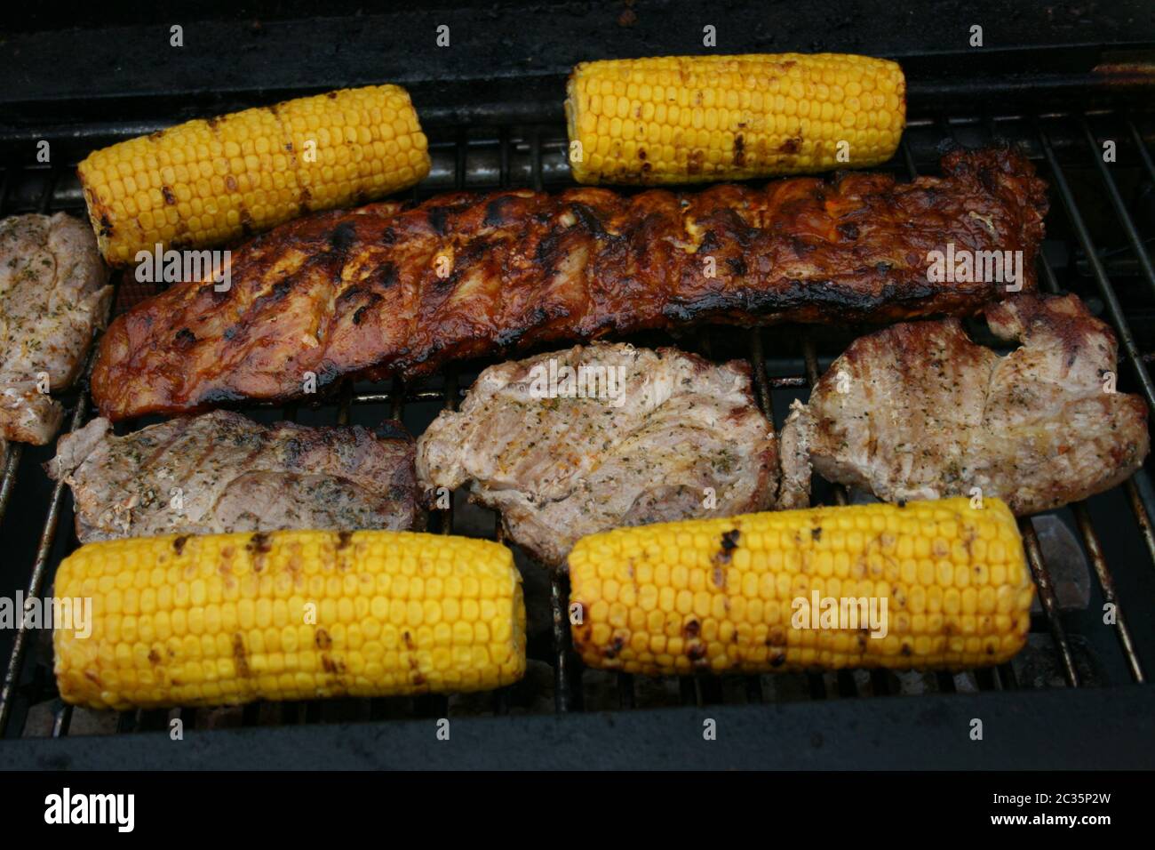 Several pieces of grilled meat and corn on the cob on a grill Stock Photo