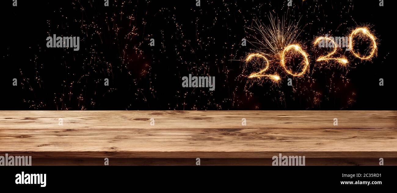 Gold sparkling new year 2020 on night sky. Background with empty wooden surface and fireworks for a concept decoration and space for text. Stock Photo