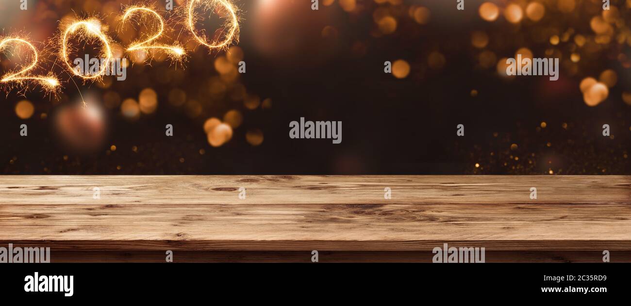 Gold sparkling new year 2020 with bokeh on night sky. Background with empty wooden surface and fireworks for a concept decoration and space for text. Stock Photo