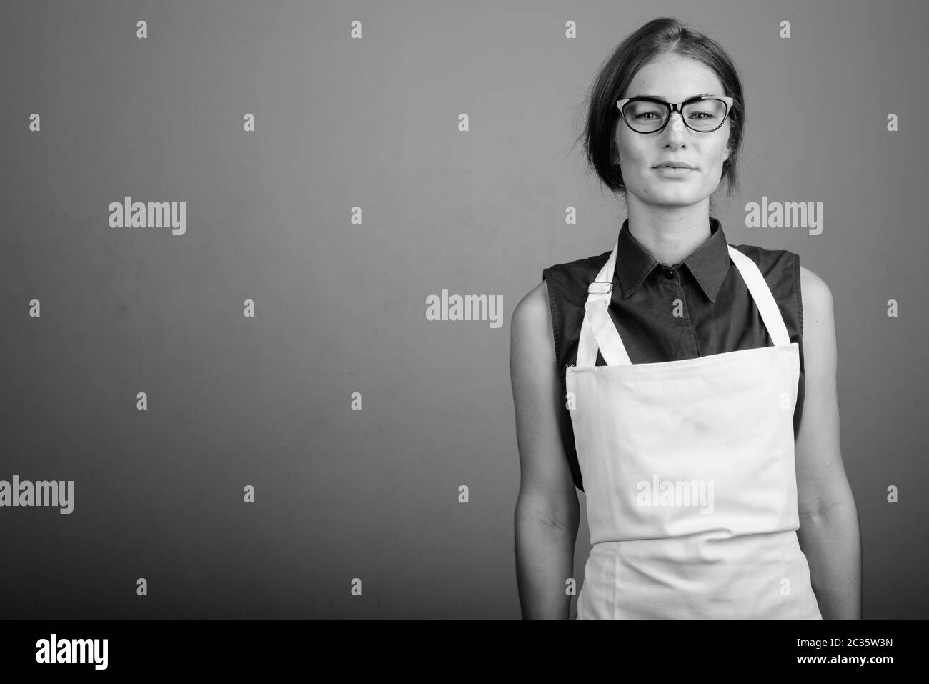 Young woman wearing apron and eyeglasses against gray background Stock ...