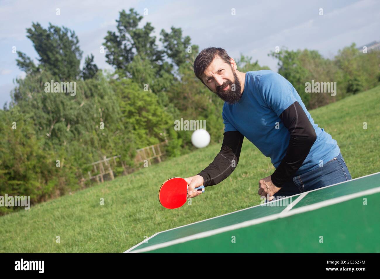 The bearded man is playing table tennis outdoors, active life concept. Stock Photo