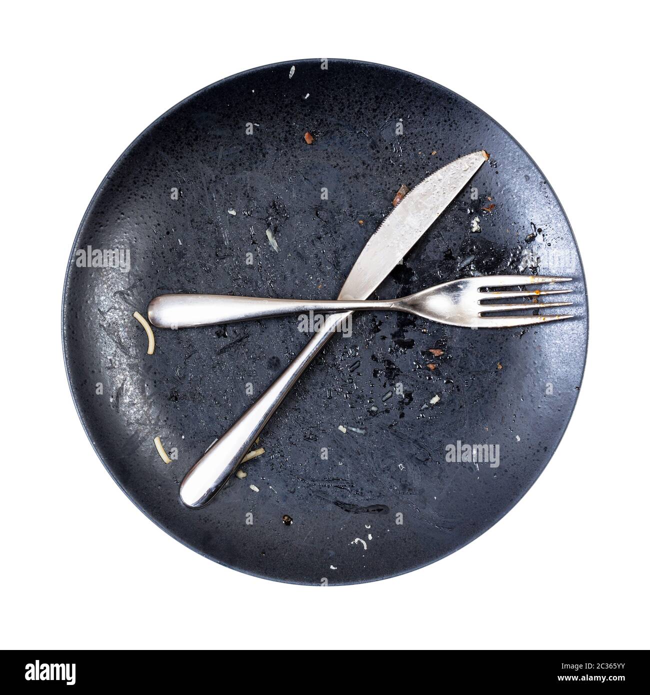 top view of crossed knife and fork on dirty black plate after lunch