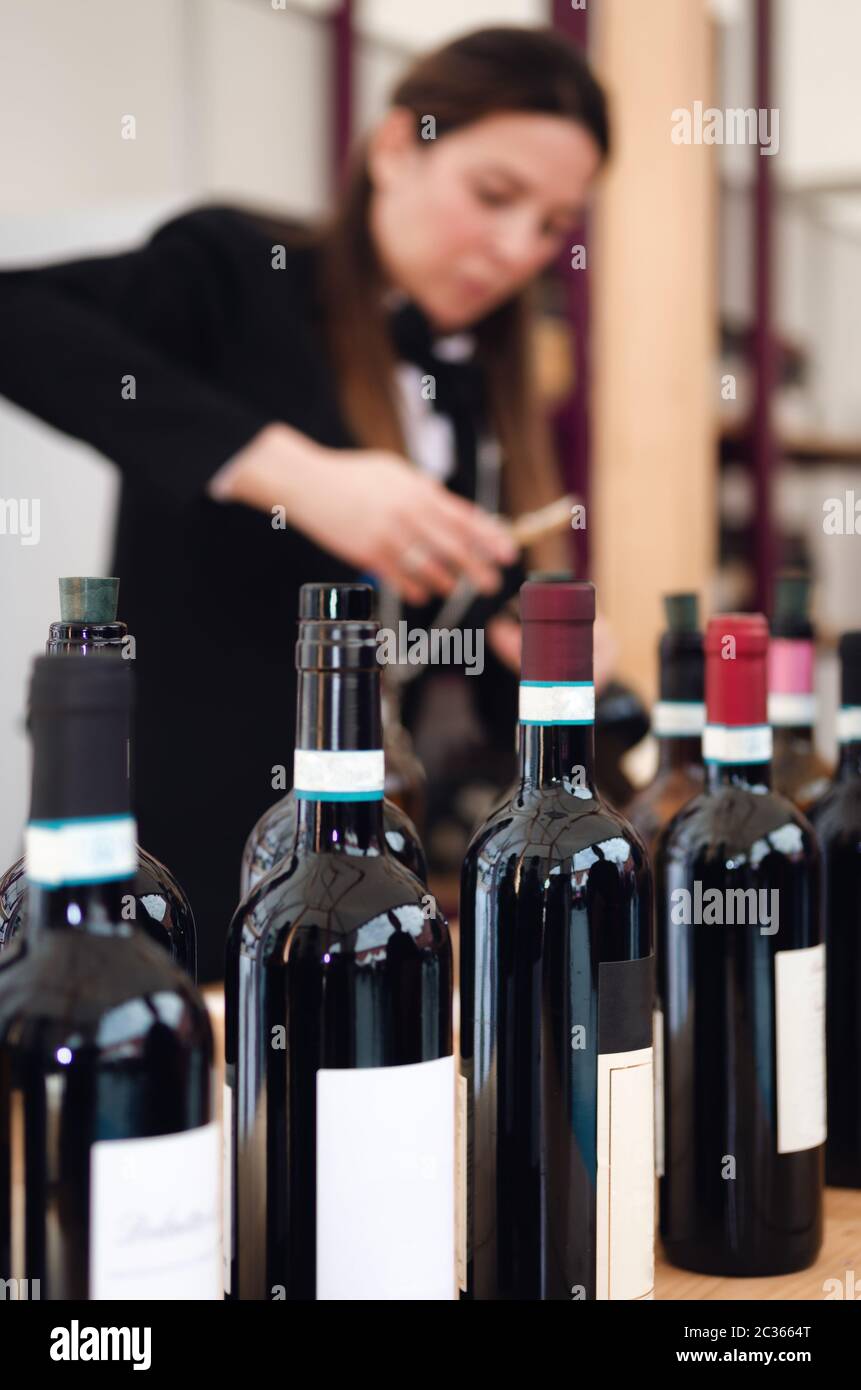 Tasting experience with bottles and an out of focus  female sommelier uncorking a bottle of red dolcetto wine in the background Stock Photo