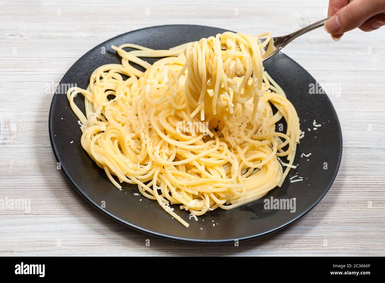 winding spaghetti al burro e parmigiano (pasta with butter and cheese) on  fork over black plate on gray wooden table Stock Photo - Alamy