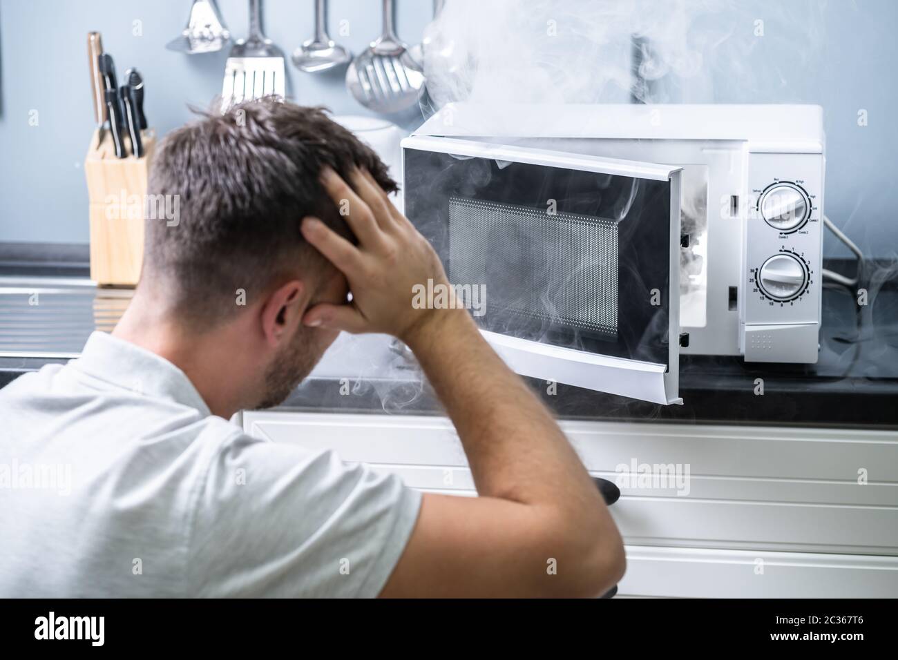Young Man Spraying Fire Extinguisher On Microwave Oven In The Kitchen