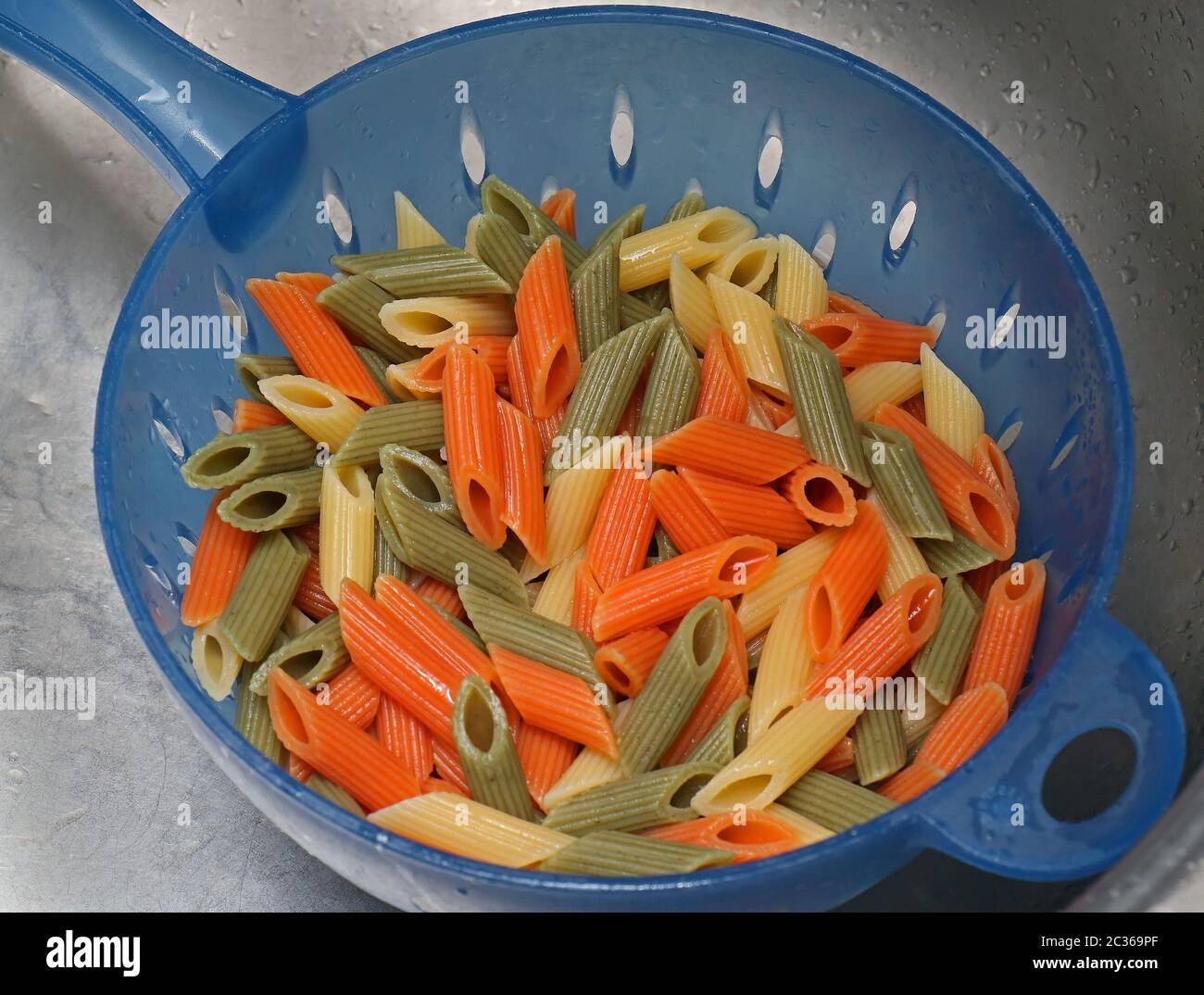 Colorful cooked penne pasta draining inside plastic strainer Stock