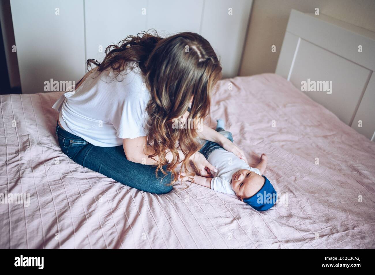 Cute little baby boy lying on pink blanket at bedroom with young mom