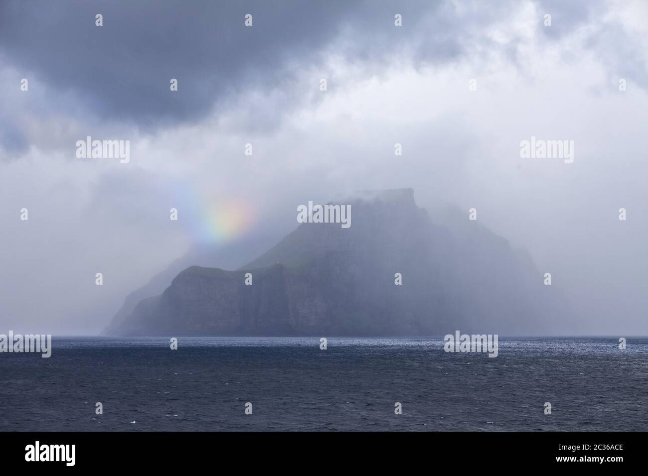 The Faeroeer island of Kalsoy in the Atlantic with a small piece of a rainbow, fog and clouds Stock Photo
