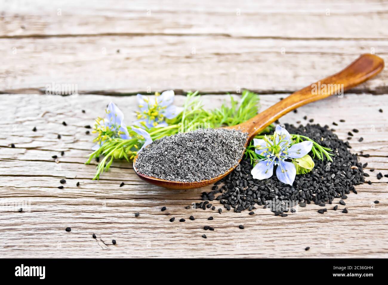 Flour of Nigella sativa in spoon with flower and leaves of kalingini on a wooden board background Stock Photo