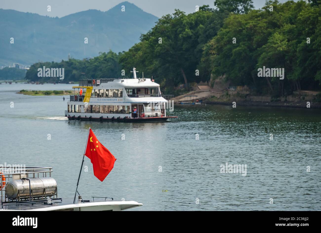 Guilin, China - August 2019 : Red Chinese national  flag fluttering on a mast on the deck of sightseeing boatt full of tourists departing on a trip on Stock Photo