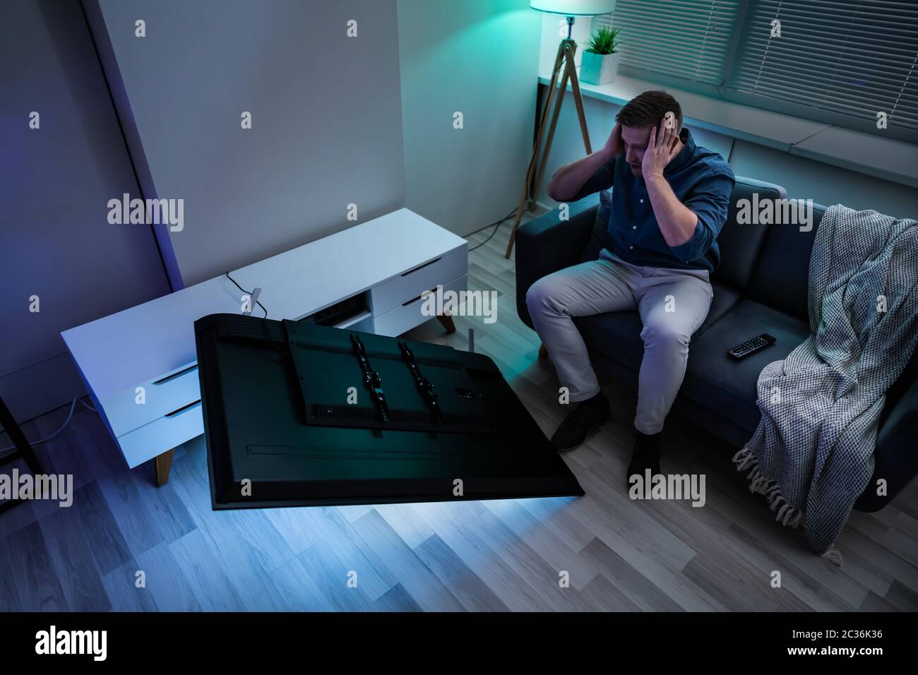 Man Sitting On Sofa In Front Fallen Television With Broken Screen Stock Photo