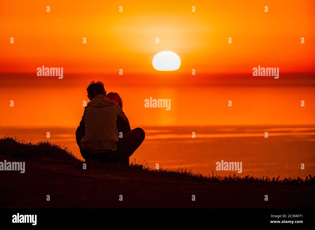A red burning sunset over the sea with the silhouette of a young couple ...