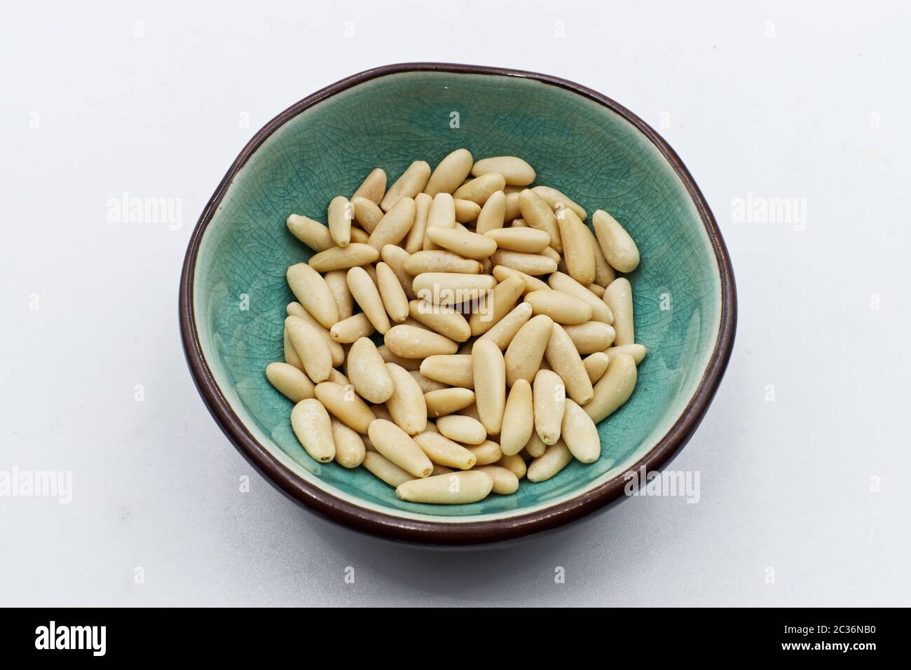 Pine nuts in ceramic bowl, isolated on white background Stock Photo