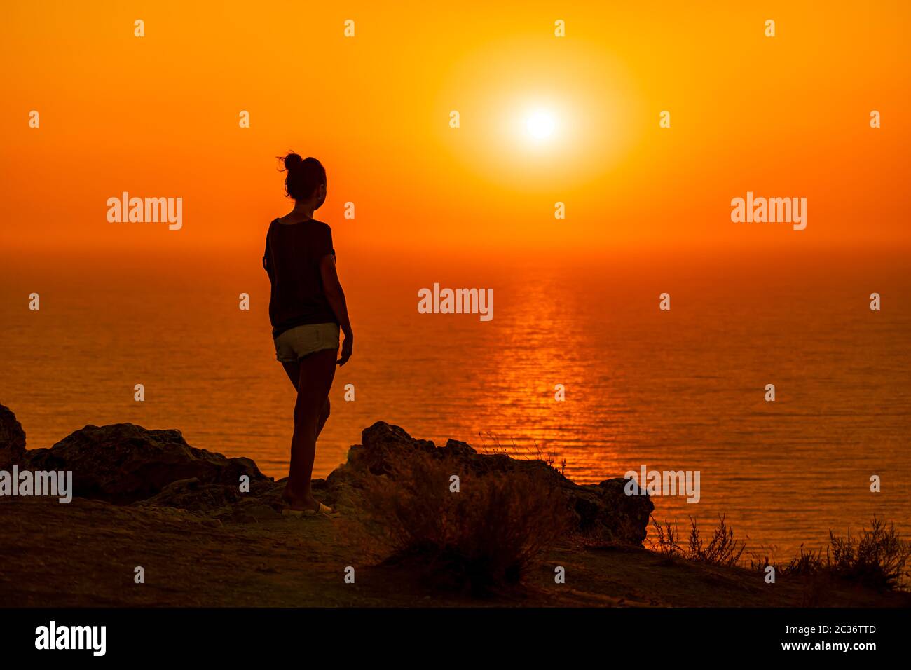 A red burning sunset over the sea with the silhouette of a young woman ...