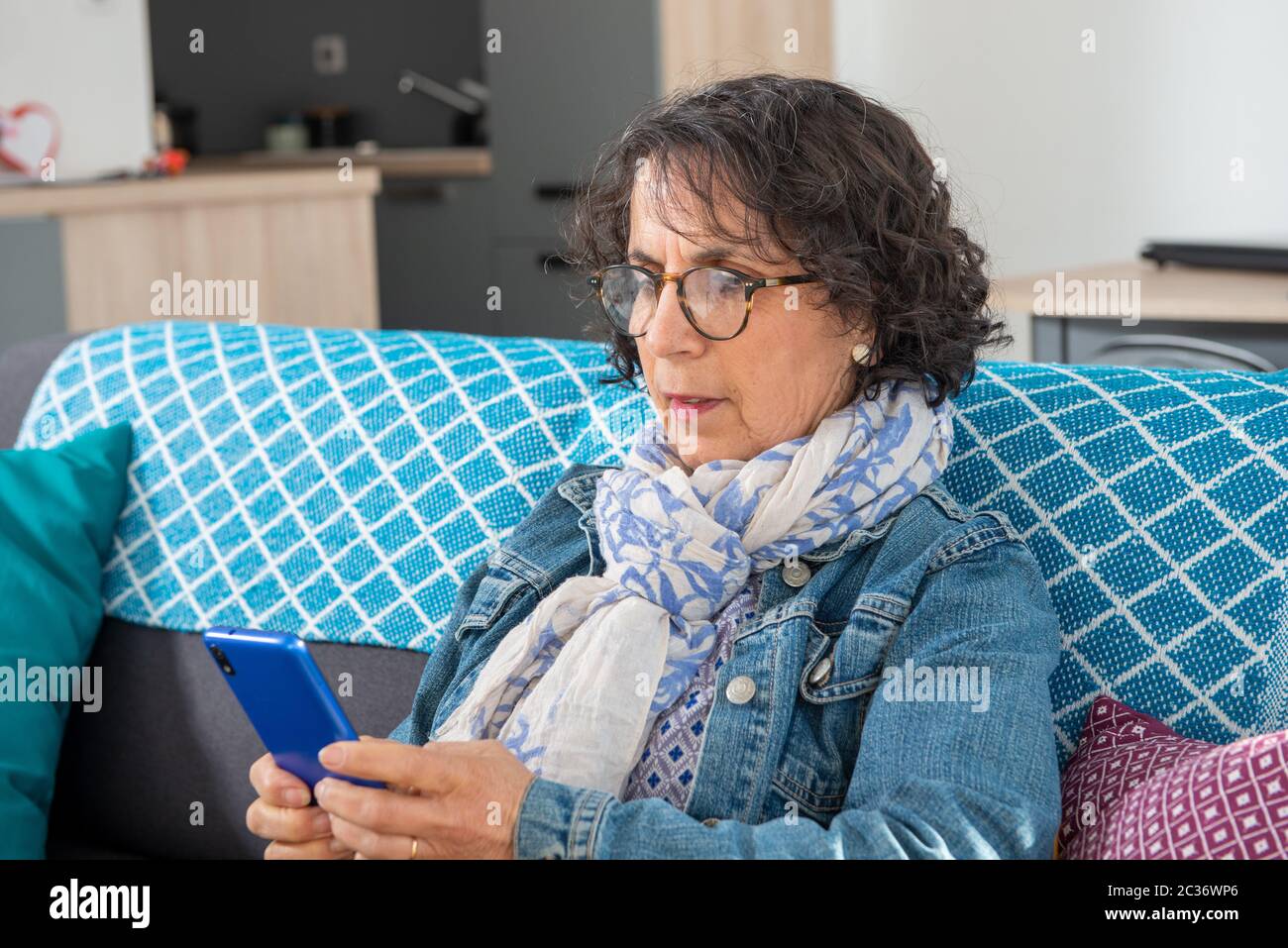 a cheerful brunette senior woman using smartphone while sitting on sofa Stock Photo
