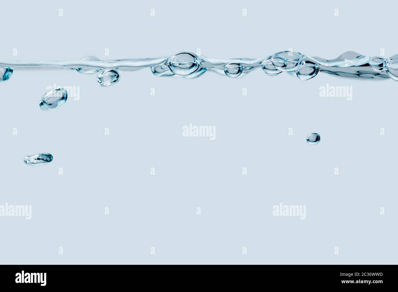 Studio shot of a series of air bubbles on the water surface with air bubbles rising underneath against a light blue background. Stock Photo
