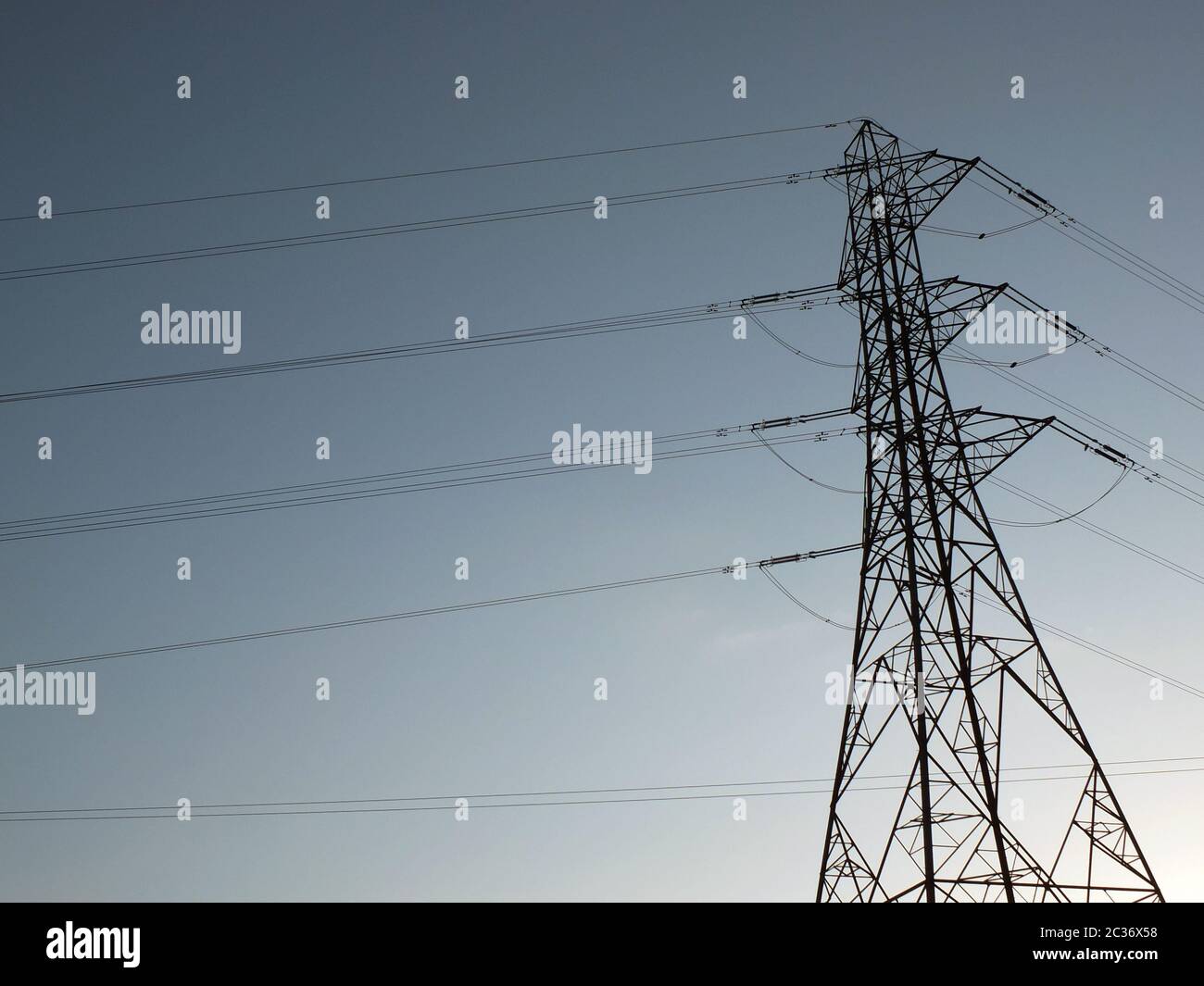 a tall electricity pylon with multiple high voltage cables silhouetted against a blue sky Stock Photo