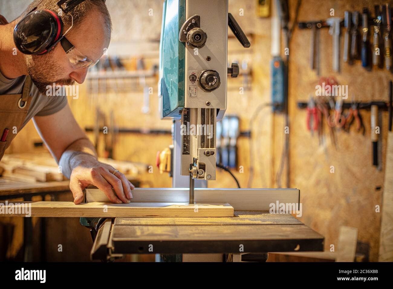 portrait of a carpenter inside his carpentry workshop using a band saw. Wear ear and eye protection Stock Photo