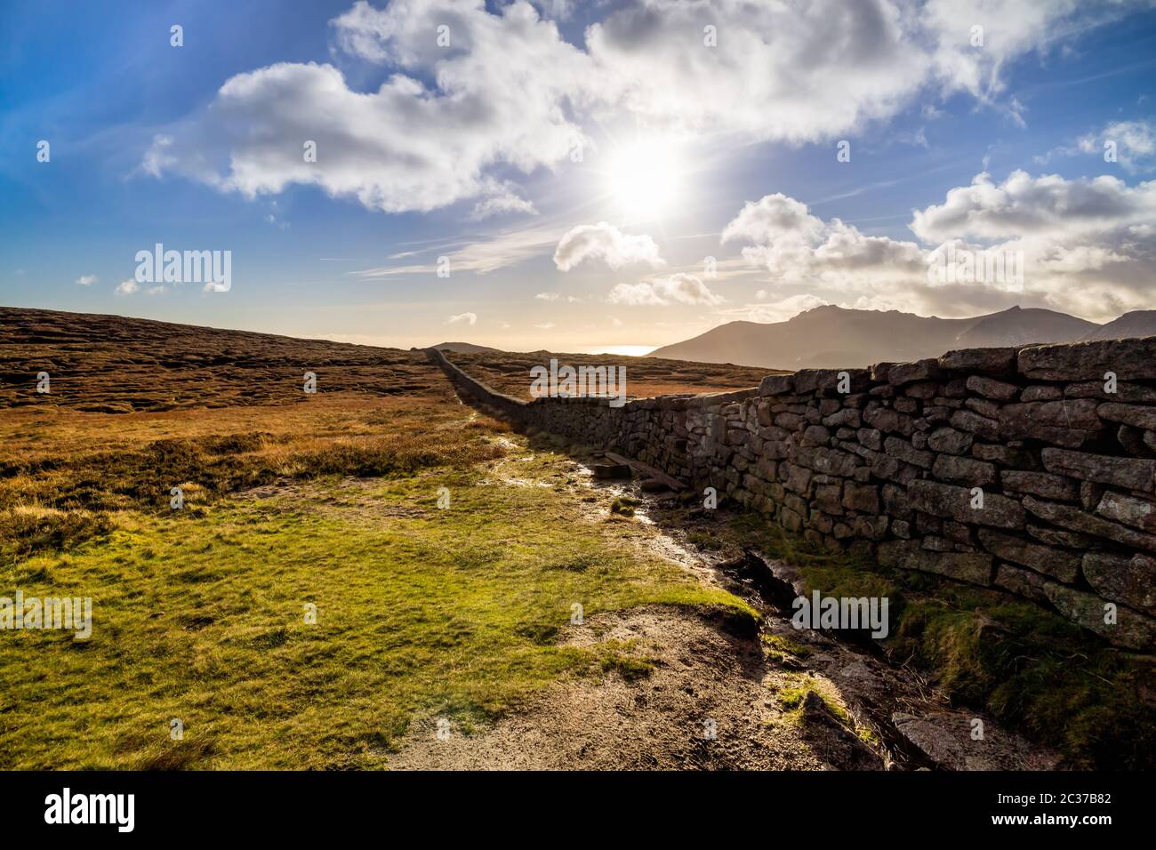 Mourn Wall on the bank of Slieve Donard mountain with blue sky, white clouds and sunrays. Stock Photo