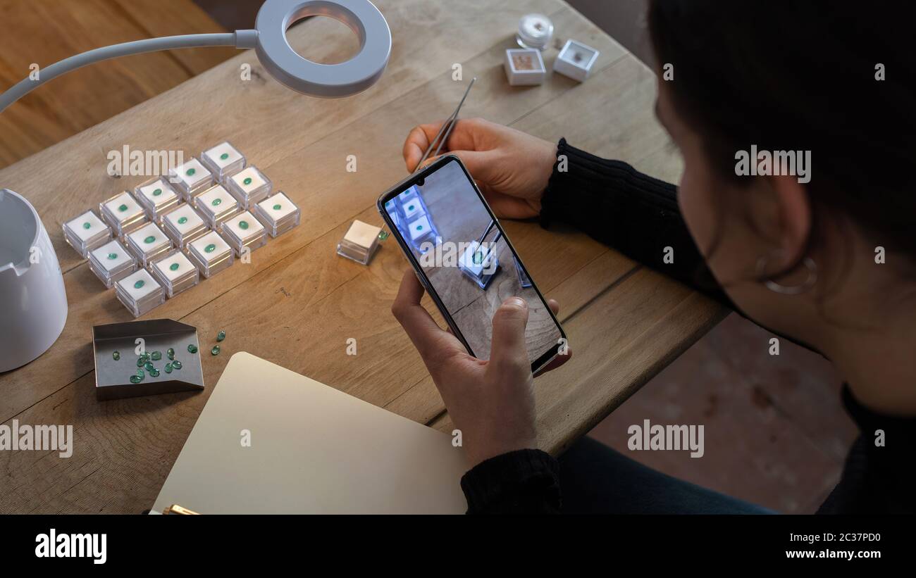 Gemologist working taking photos of precious emerald stones with her mobile phone. Work space. Stock Photo