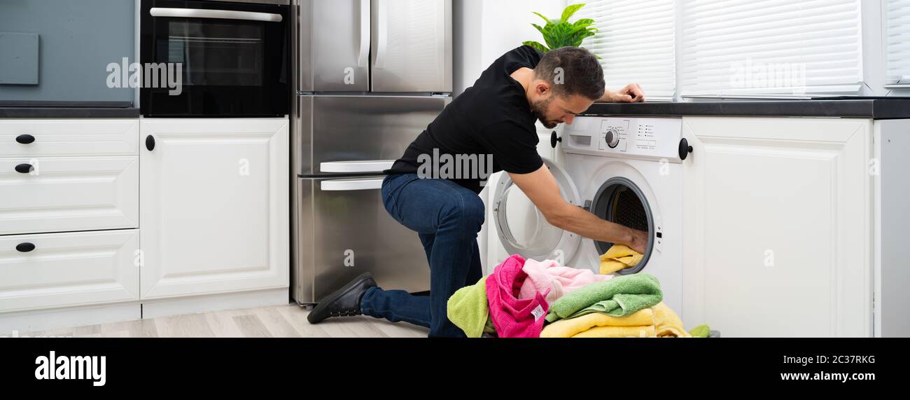 Man Loading Clothes Into Washing Machine In Kitchen Stock Photo