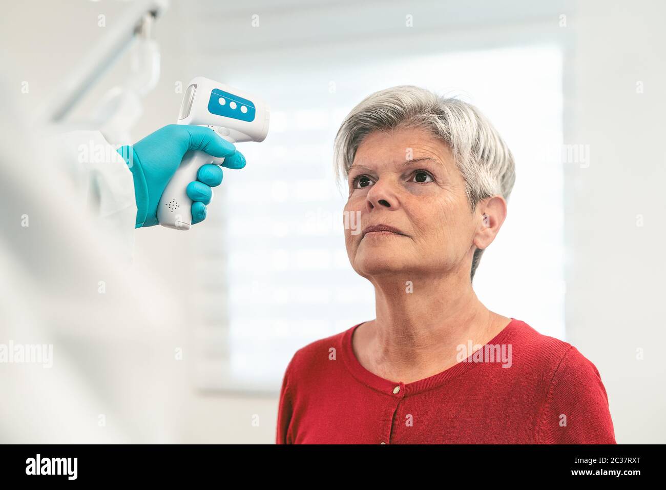 Doctor measuring temperature with new digital thermometer to senior woman patient during corona virus pandemic Stock Photo