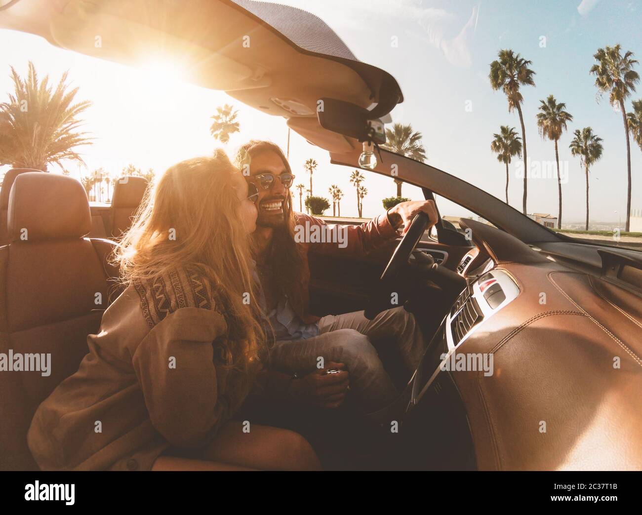 Happy young couple doing road trip in tropical city - Travel people having fun driving in trendy convertible car discovering new places Stock Photo