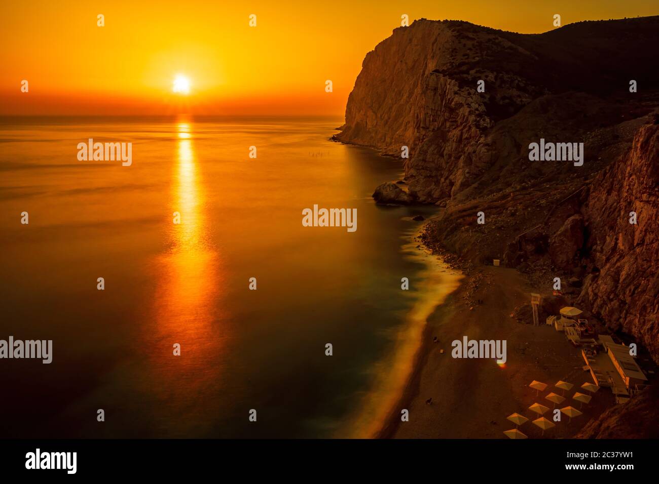 A red burning sunset with the silhouette of a cliff over a beach. Long ...