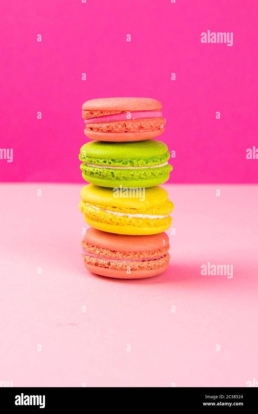 Multi-colored macaroons stand in a pile on a pink table. Close-up Stock Photo