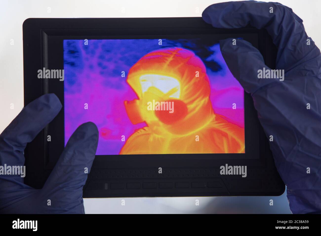 Thermal camera view of an unrecognizable person with a face mask. Hands with dark blue plastic gloves are holding the monitor. Corona Covid 19 theme f Stock Photo