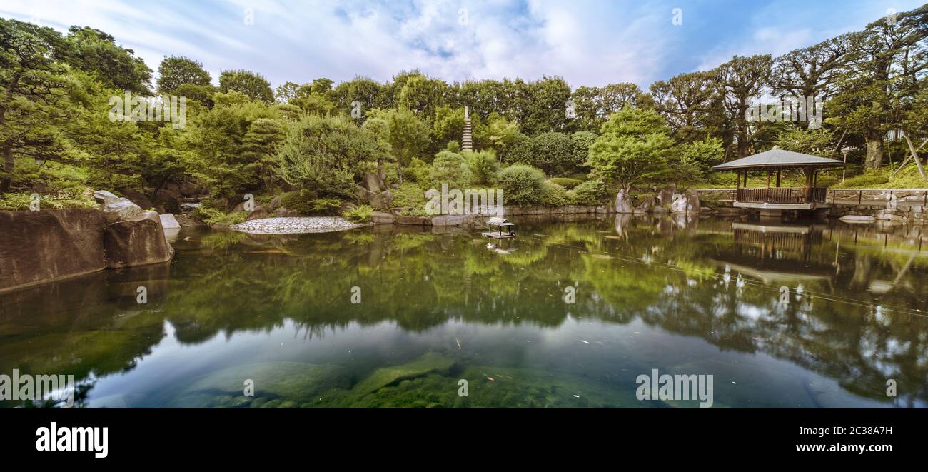 Central pond of Mejiro Garden which is surrounded by large flat stones under the foliage of the momi Stock Photo