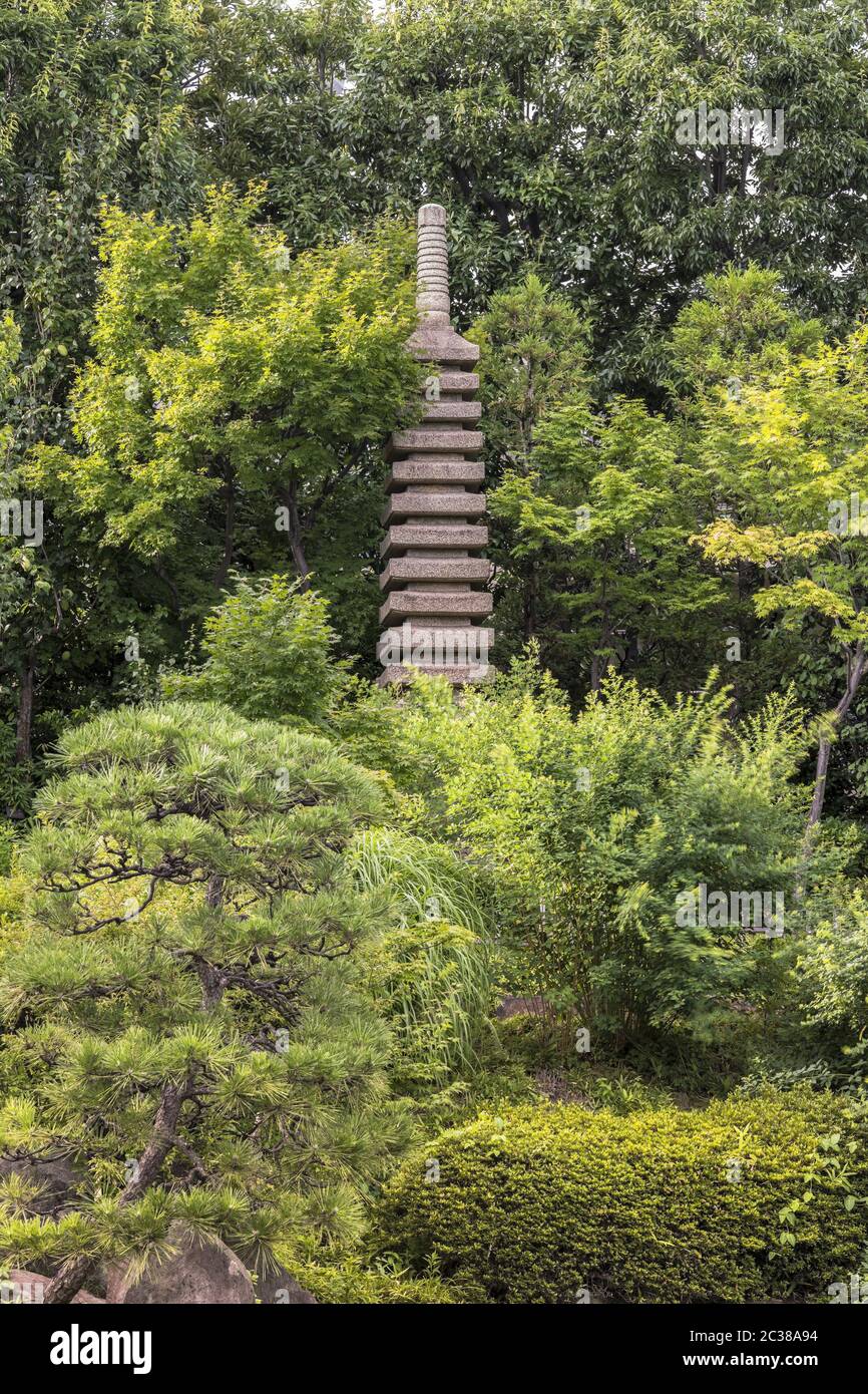 Stone tower pagoda in front of the central pond of Mejiro Garden which is surrounded by large flat s Stock Photo