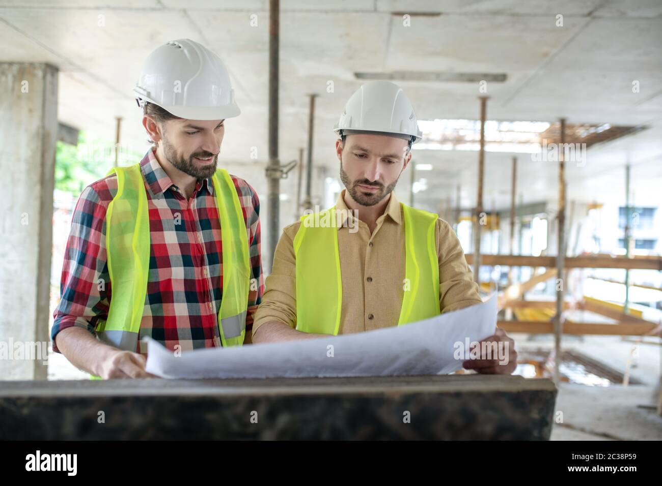 Building site. Building workers brainstorming over blueprint, discussing it Stock Photo