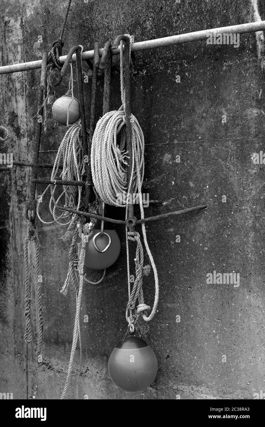Buoys and ropes hanging against a concrete wall in black and white Stock Photo