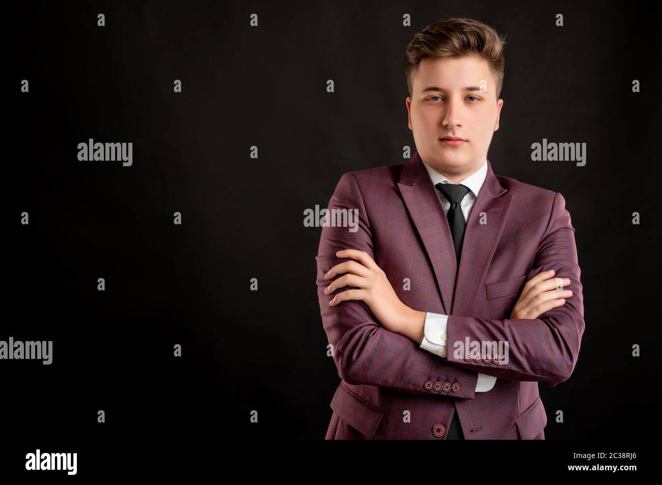 Law student with blond hair dressed in burgundy jacket, white shirt and black tie looking confident posing on isolated black background with copy spac Stock Photo