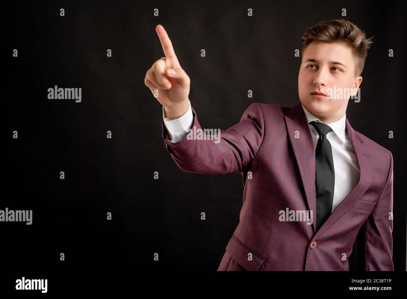 Law student with blond hair dressed in burgundy jacket, white shirt and black tie presses a virtual button posing on isolated black background with co Stock Photo
