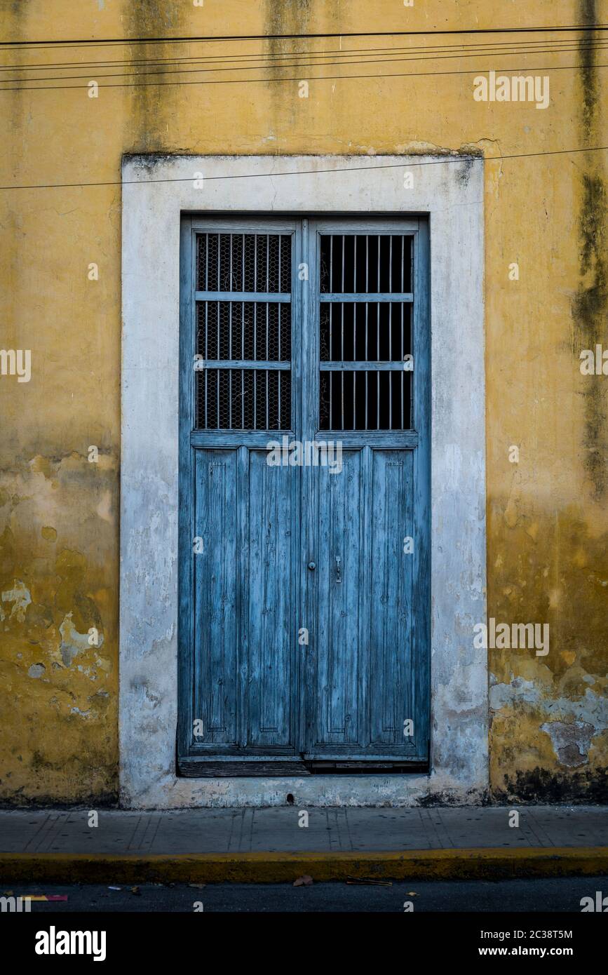 Blue wooden door on a yellow run down facade, Merida, Mexico Stock Photo