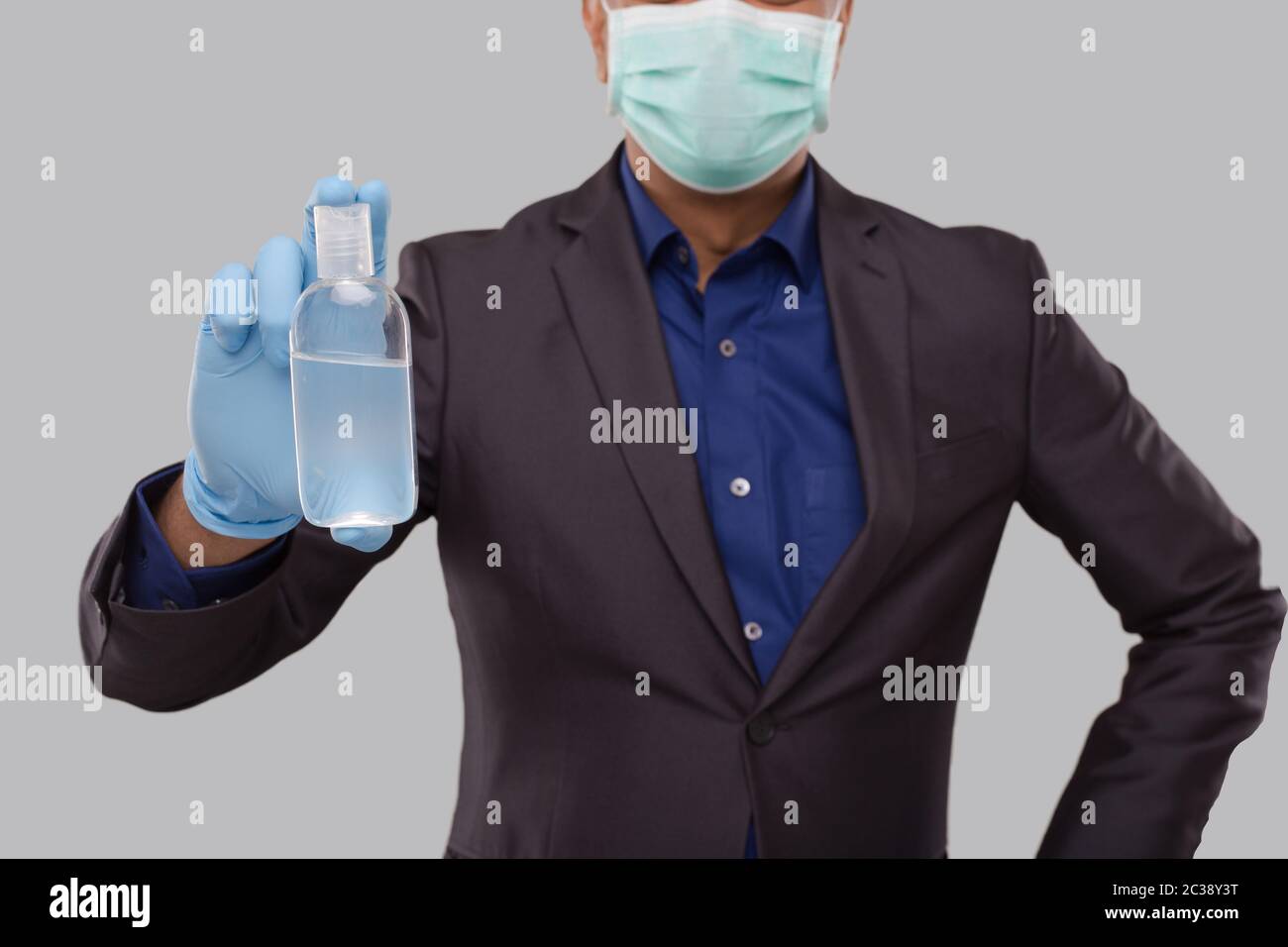 Businessman Showing Hands Sanitizer Wearing Medical Mask and Gloves Close Up. Indian Business man Holding Hand Antiseptic Stock Photo