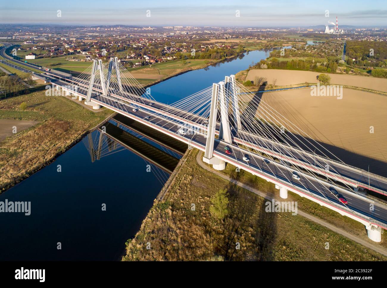 New modern double cable-stayed bridge with wide three-lane roads over Vistula River in Krakow, Poland, and its reflection in water at sunrise. Part of Stock Photo