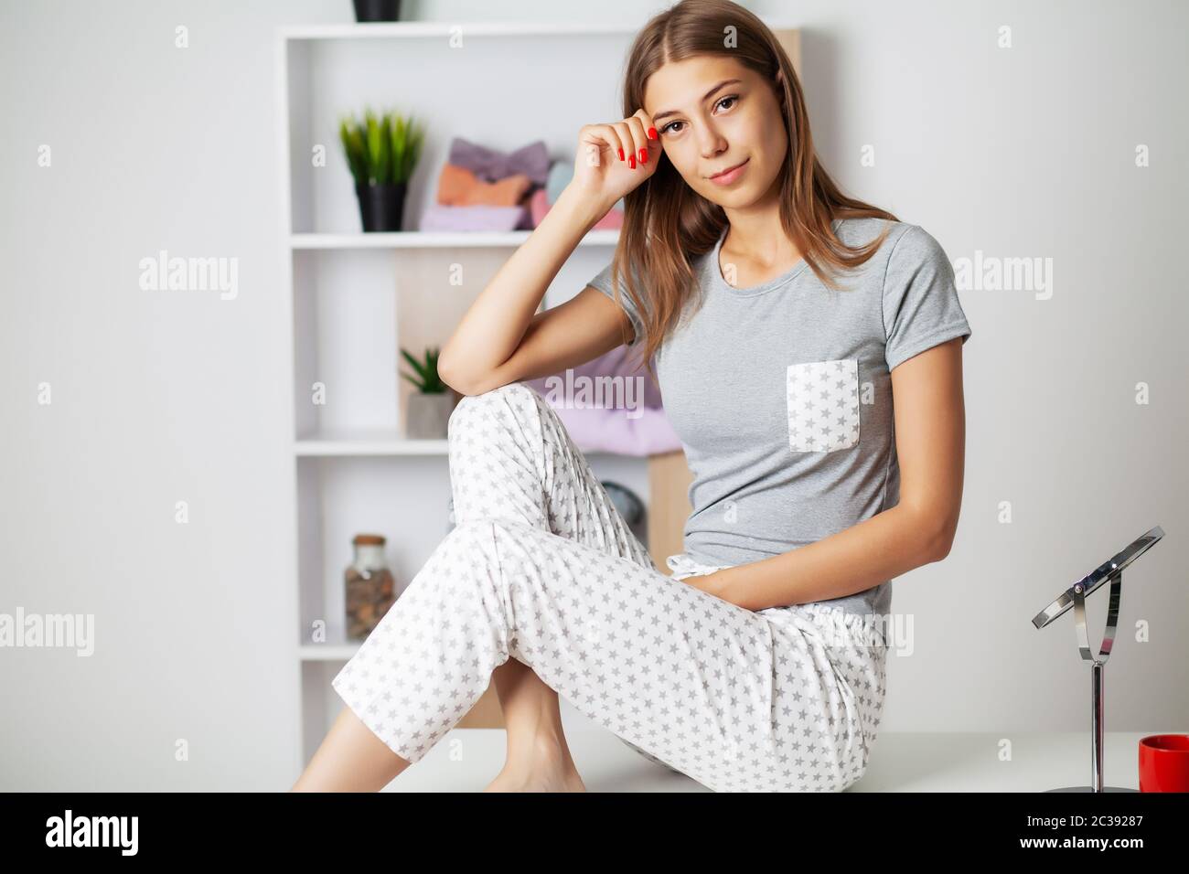Young woman in comfortable pajamas sitting on the table in her room Stock Photo Alamy