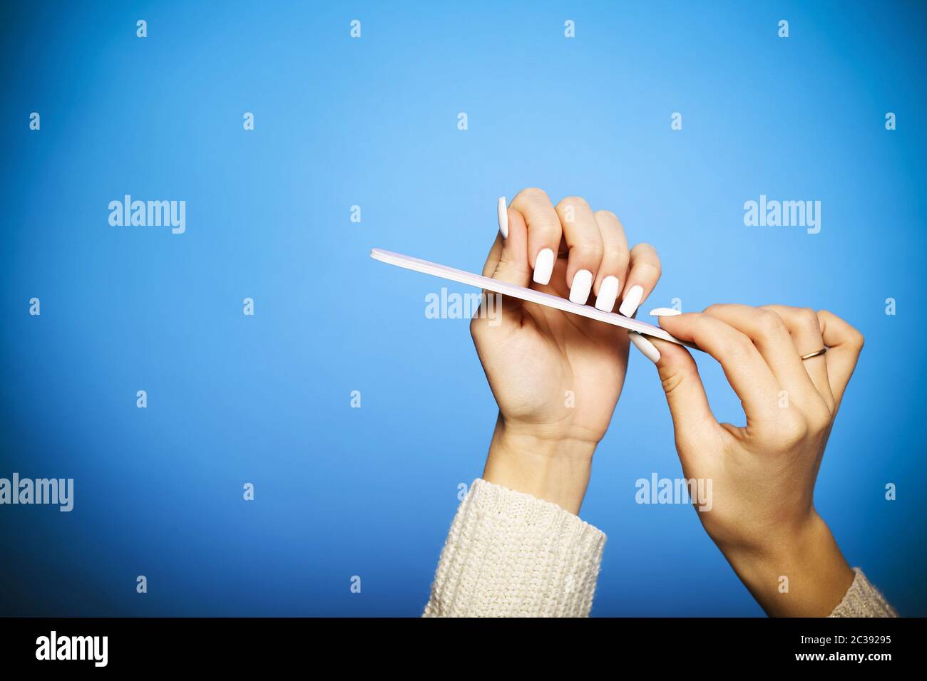 Crop woman filing long nails on blue backdrop Stock Photo