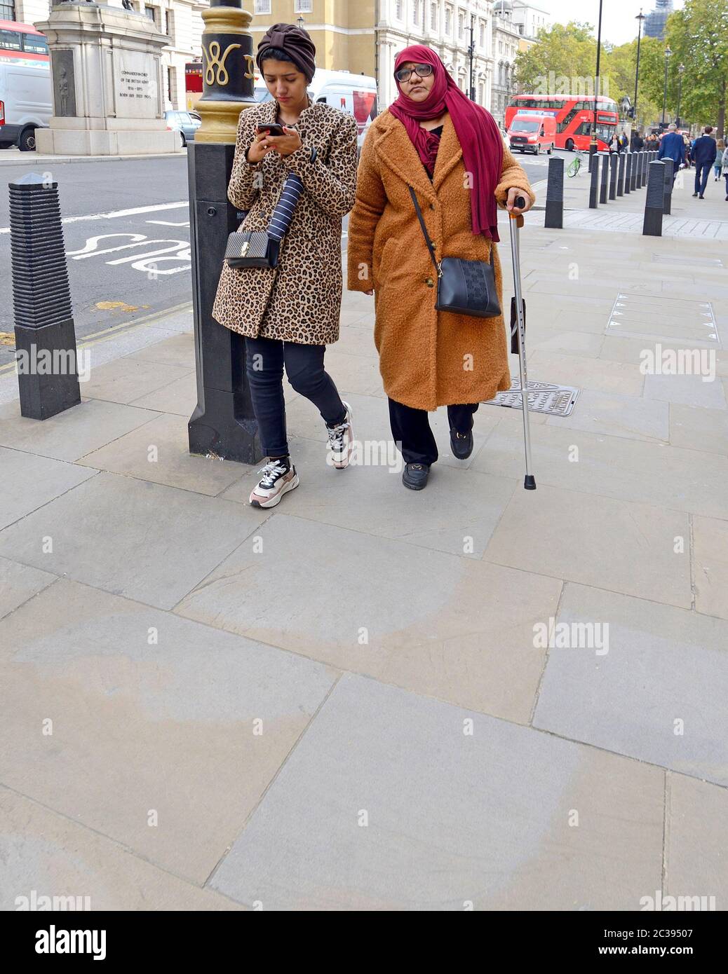London, England, UK. Old and young women walking in Whitehall - younger woman looking at her phone Stock Photo