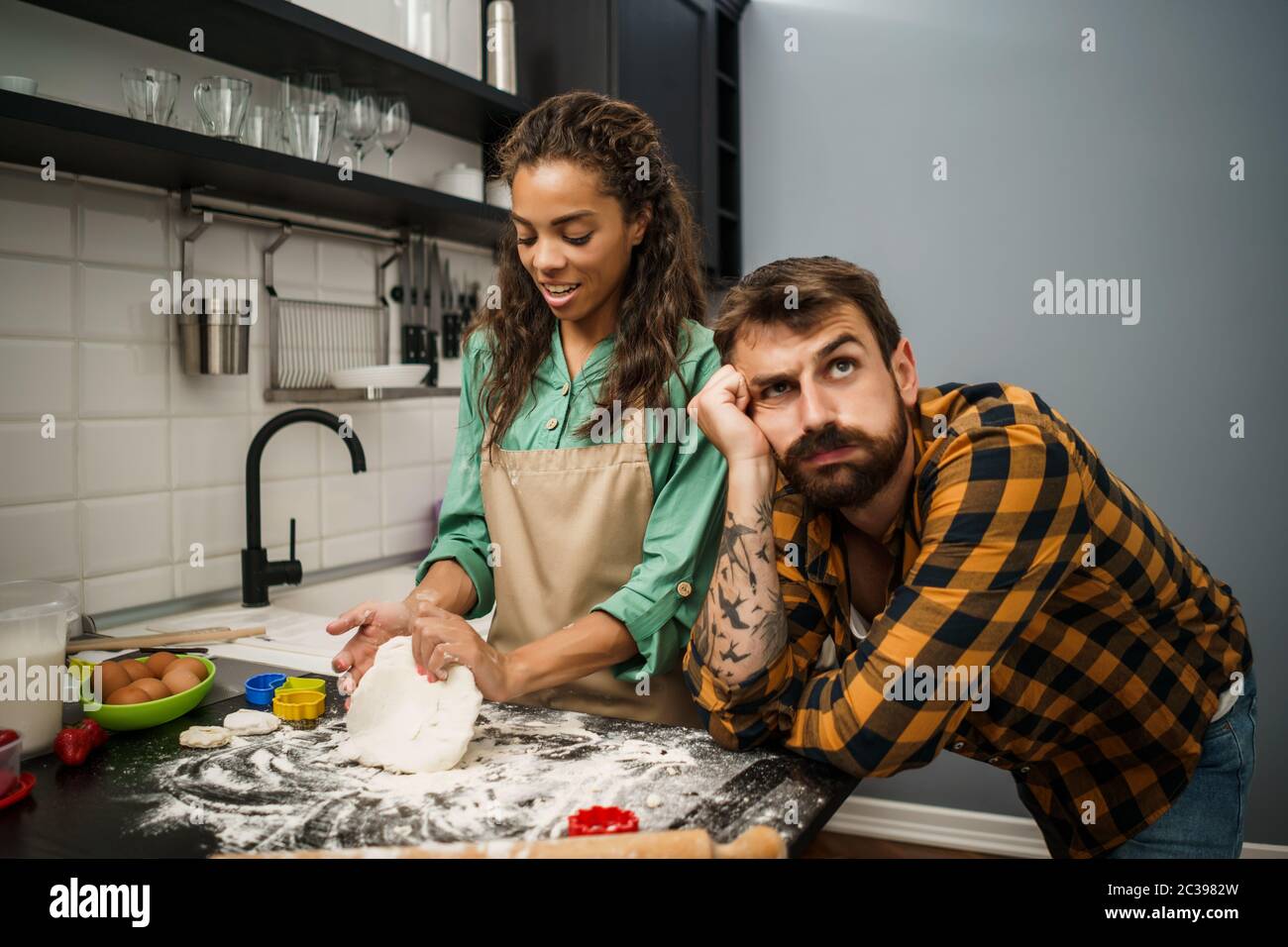 Young multiethnic couple cooking in their kitchen. They are making cookies. Stock Photo