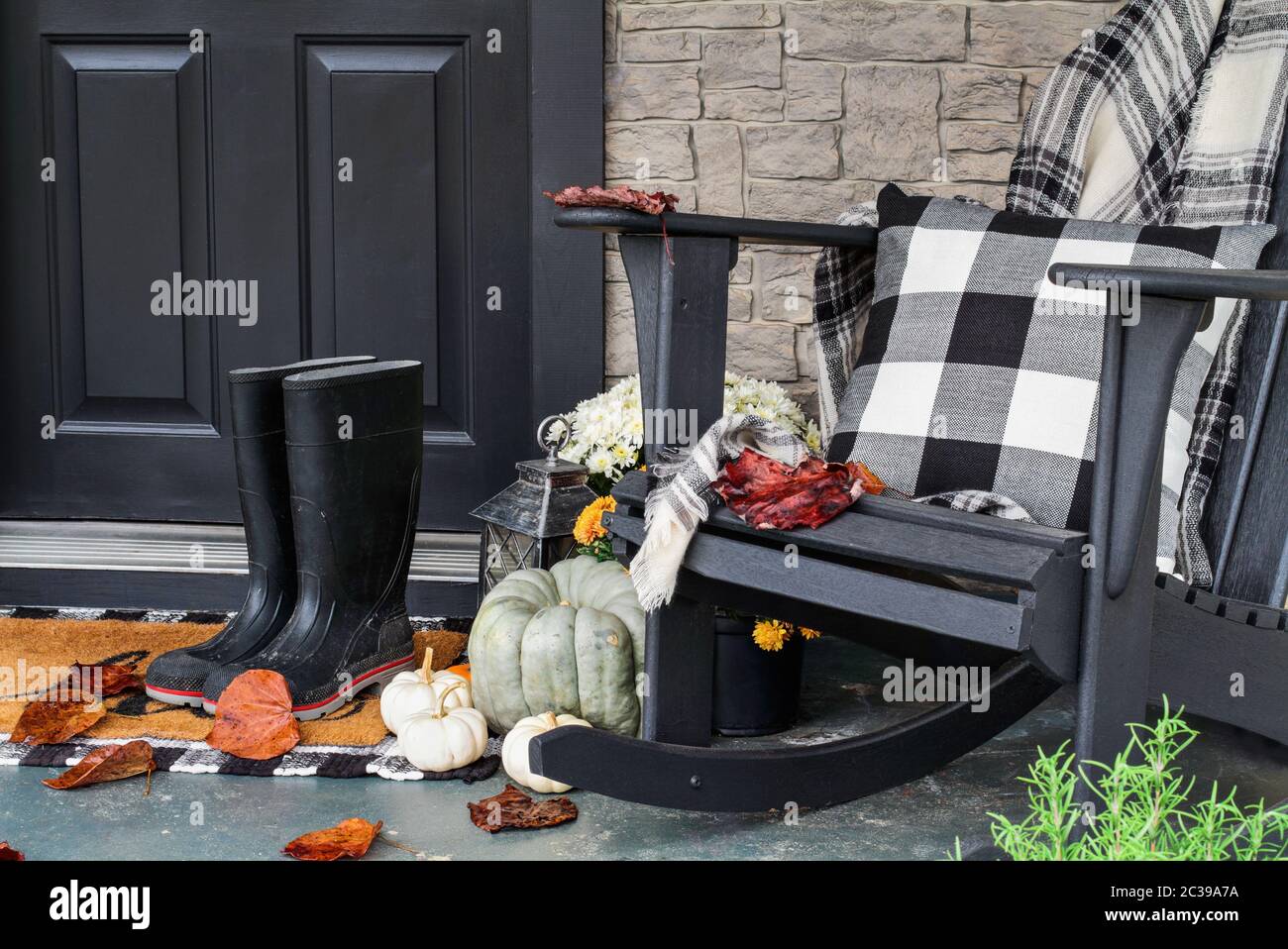 Traditional style front porch decorated for autumn with rain boots, heirloom gourds,  white pumpkins, mums and rocking chair with buffalo plaid pillow Stock Photo