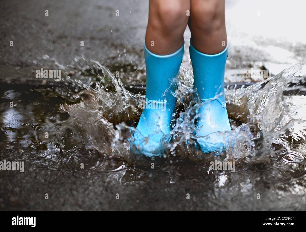 Child wearing blue rain boots jumping into a puddl Stock Photo