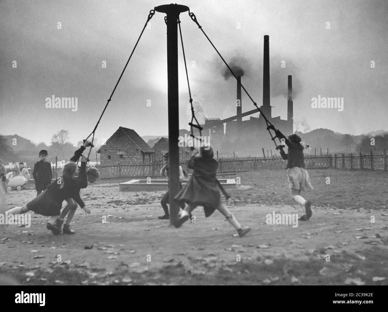 Children play on a playground in the Ruhr area. In the background, the chimneys and clouds of smoke of the industries. Stock Photo