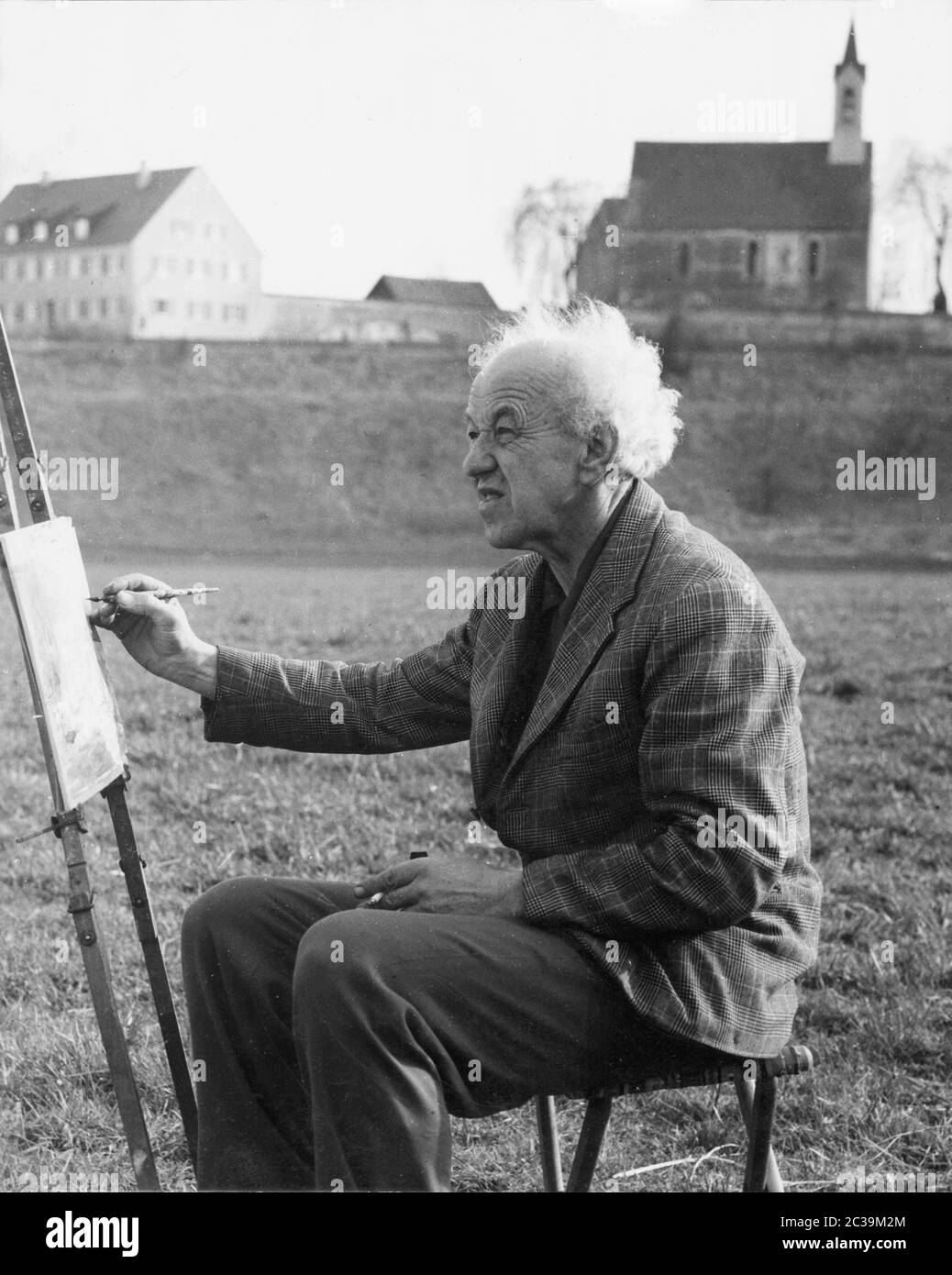 An old man sits in a meadow and paints. Undated photo. Stock Photo
