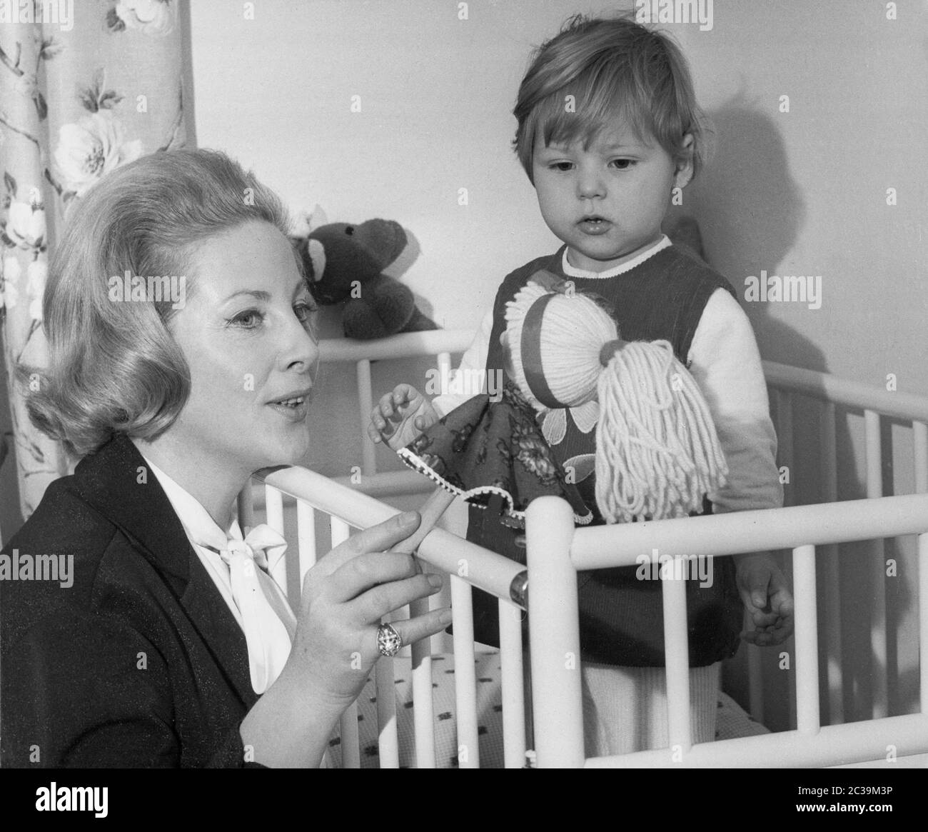 A mother and her little daughter play with a doll in a cot. Undated photo. Stock Photo