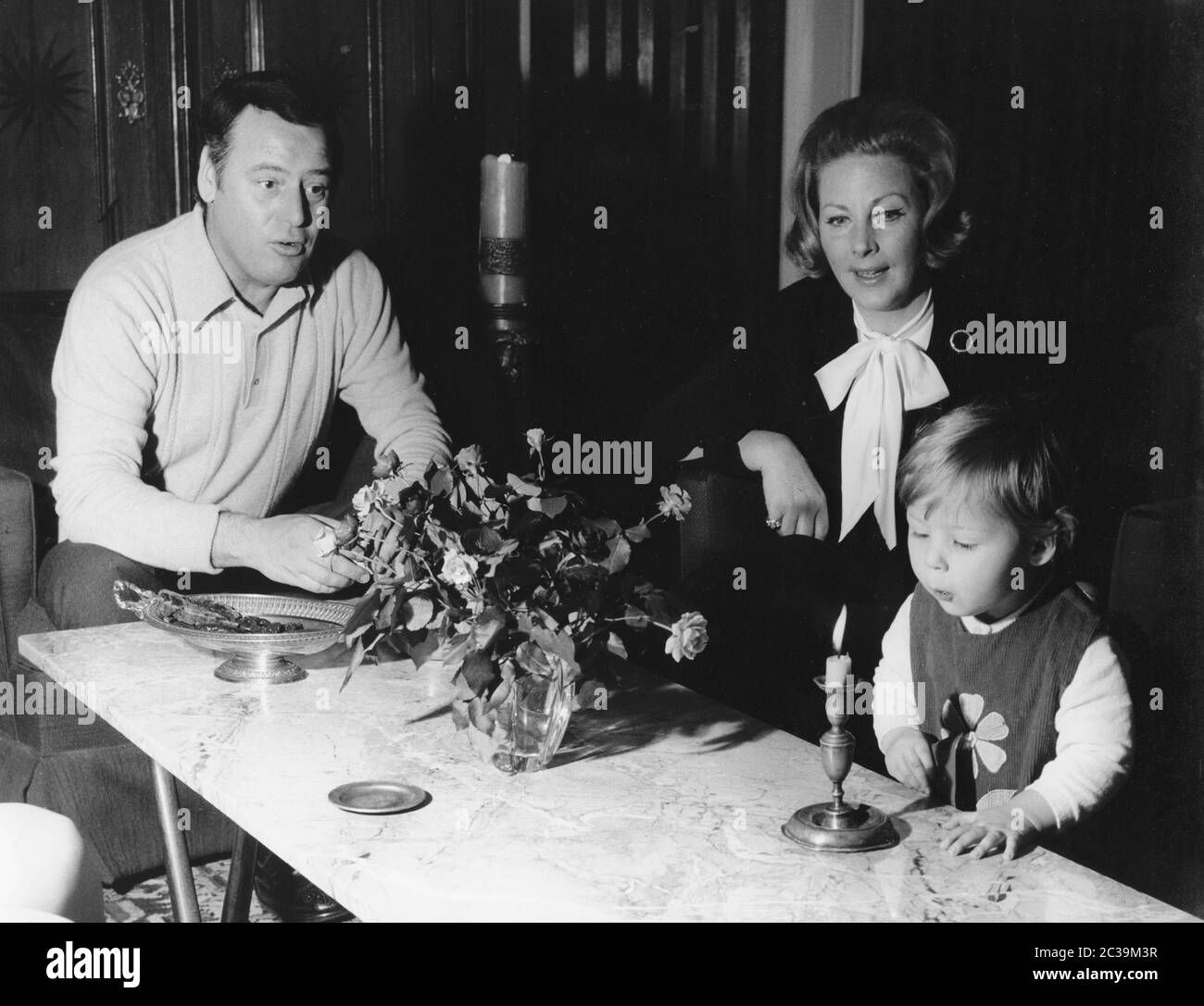 Father, mother and child sit at the dining table and the child blows out a candle. Undated photo. Stock Photo