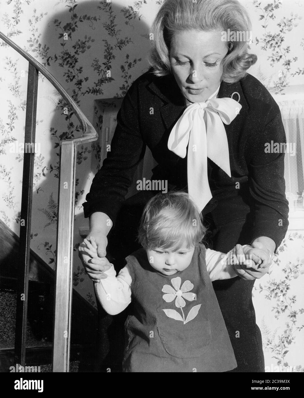 A mother walks down the stairs while holding her little daughter by the hand. Undated photo. Stock Photo
